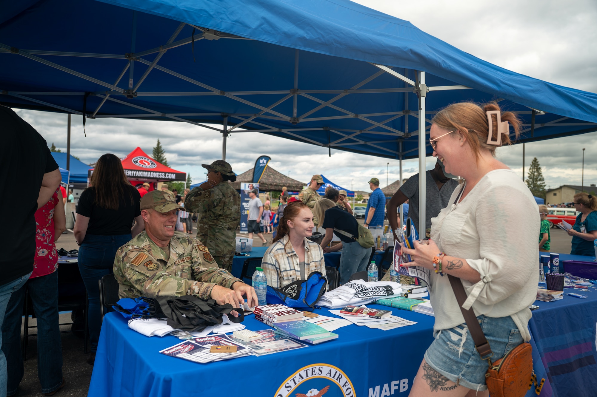 A uniformed man sits at a booth and speaks with a woman during an event.