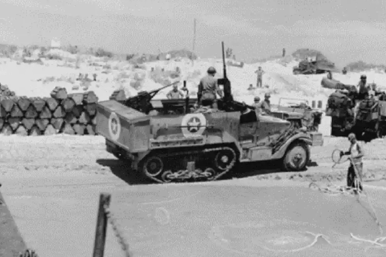 U.S. service members, some on foot and others in mechanized vehicles, outside during World War II.