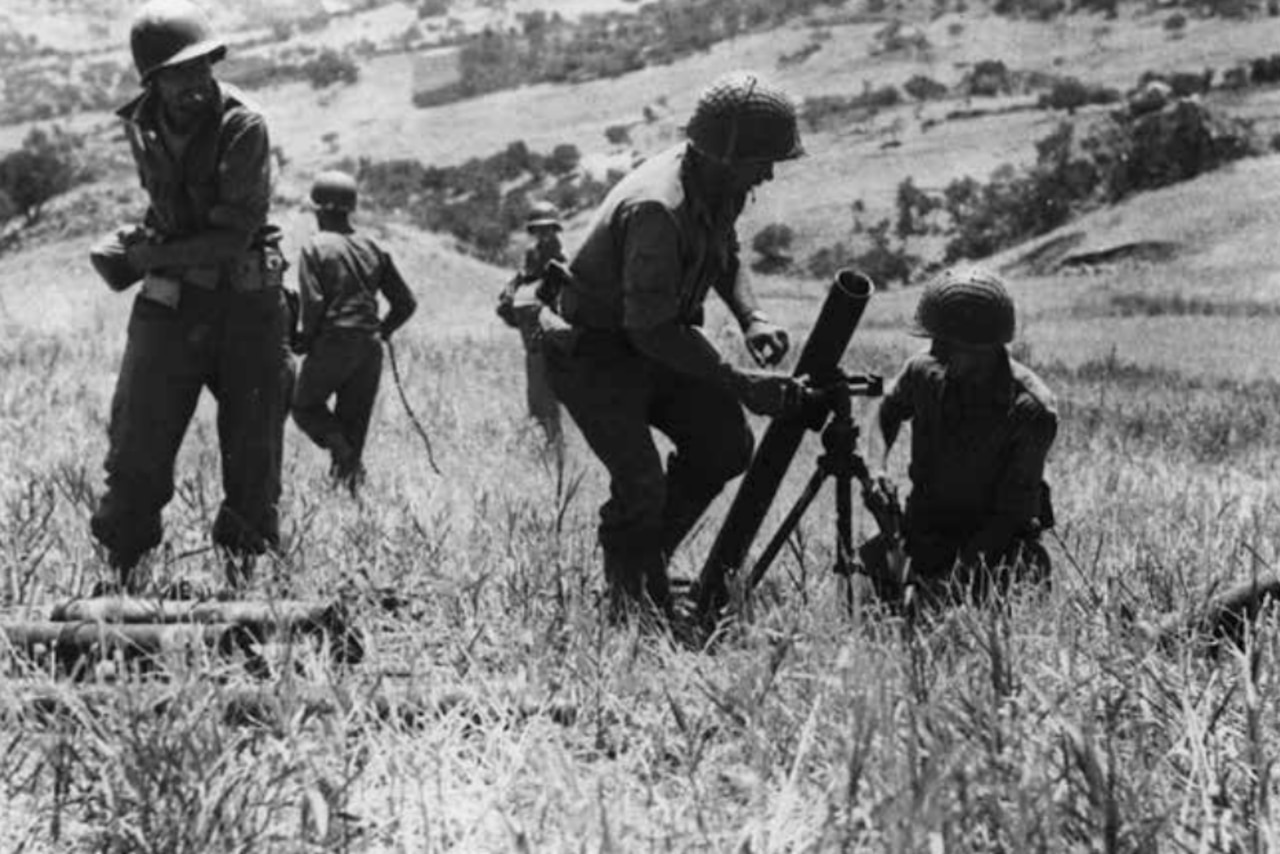 Troops on a grassy hillside set up a gun emplacement.