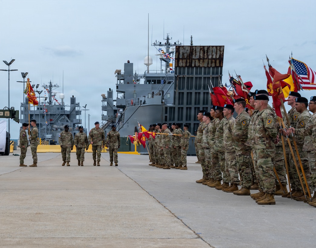 Four soldiers march past a formation of other soldiers.