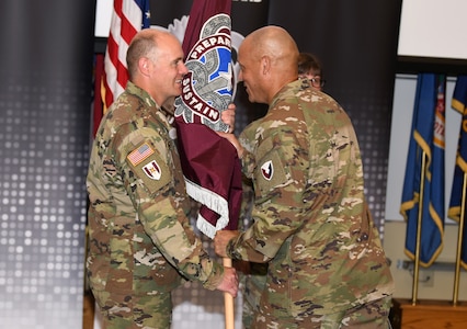 Col. Deon Maxwell, commander of U.S. Army Medical Logistics Command, passes the unit colors to Command Sgt. Maj. Andrew DeCola.