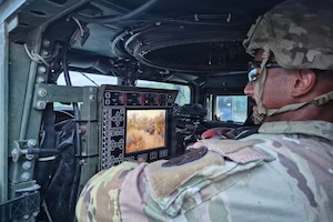 A man in a camouflage military uniform looks at a screen inside a military vehicle.
