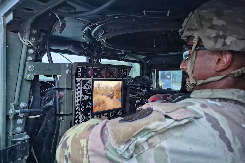 A man in a camouflage military uniform looks at a screen inside a military vehicle.