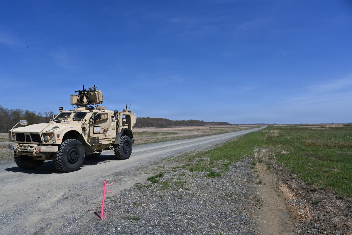 A military vehicle is parked on a gravel road in a grassy field.