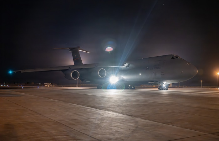 A large military cargo aircraft taxi on a tarmac at night.