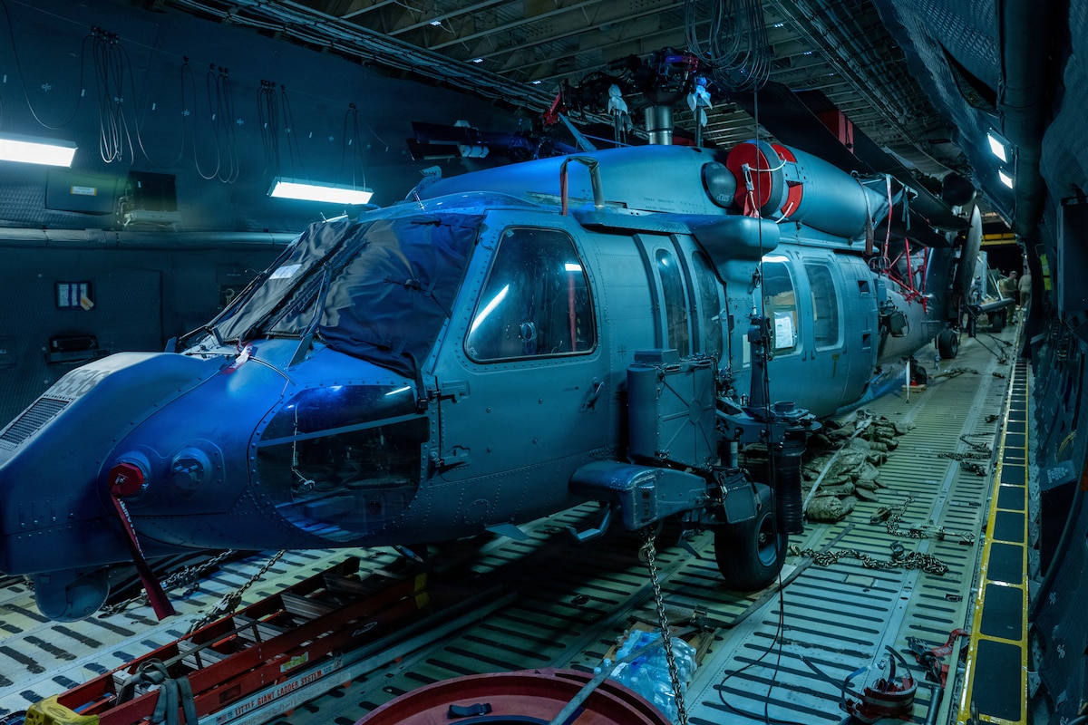 A military helicopter sits inside the cargo bay of a larger military aircraft at night.