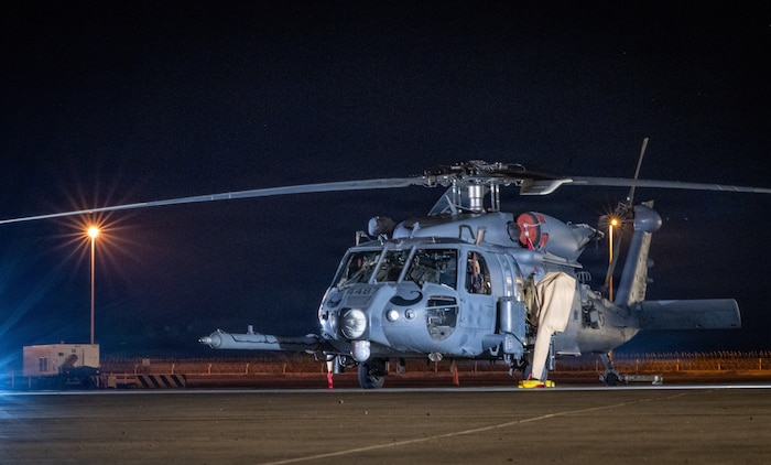 A military helicopter sits on a tarmac at night.