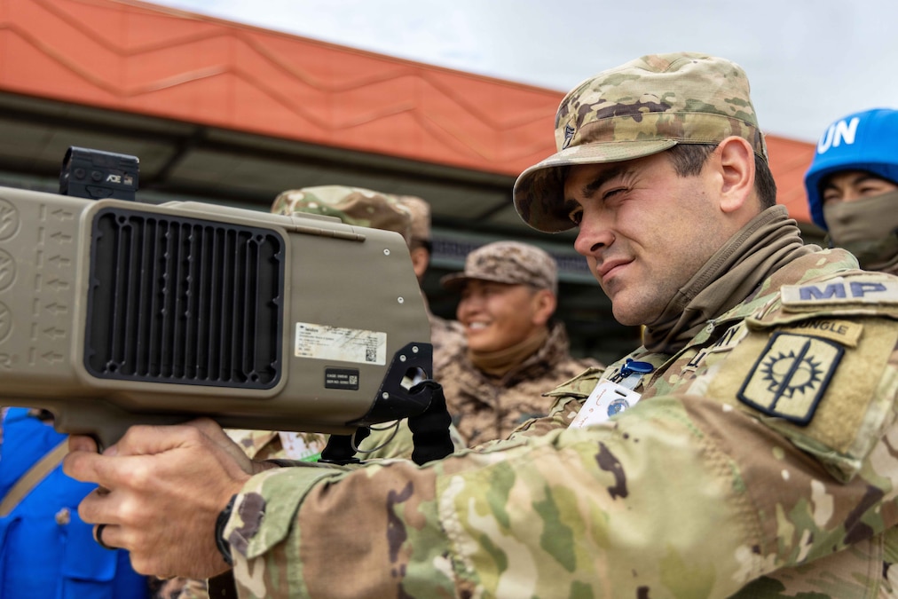A soldier uses a Dronebuster during the day as fellow service members gather behind and watch.