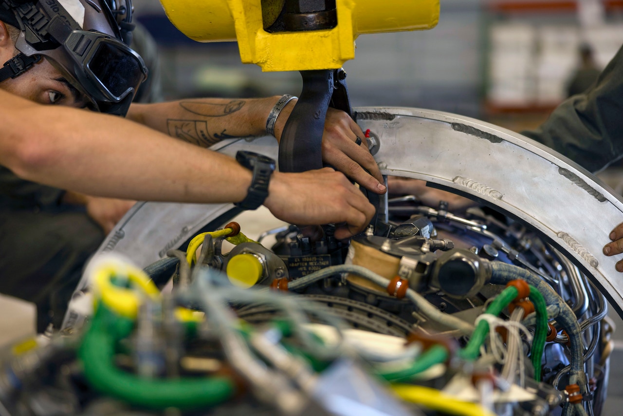 A Marine handles components of an aircraft engine.