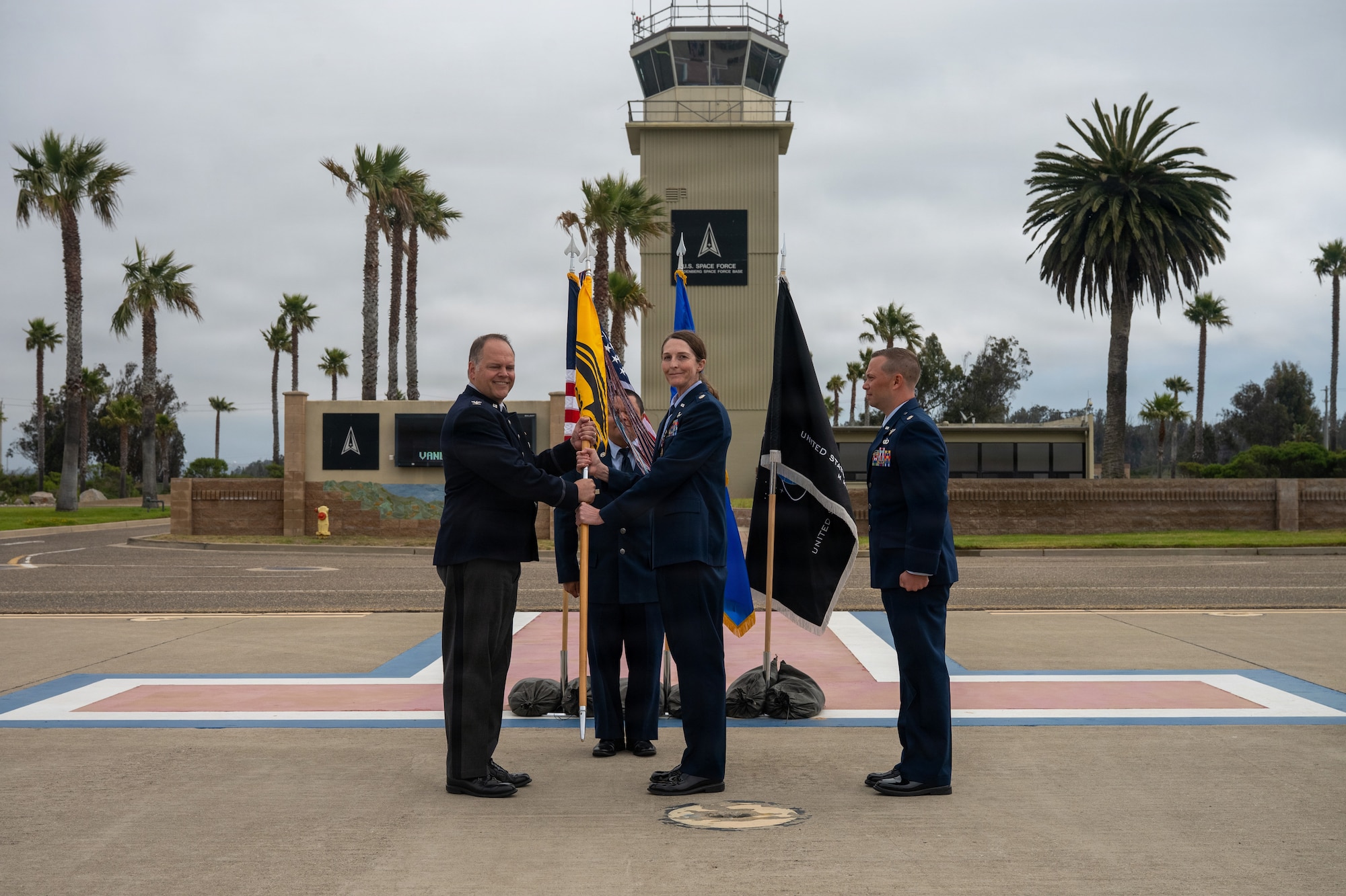 On an airfield with palm trees in the background the commander of Vandenberg receives the 30th OSS guidon from the squadron commander with the incoming squadron commander standing behind.
