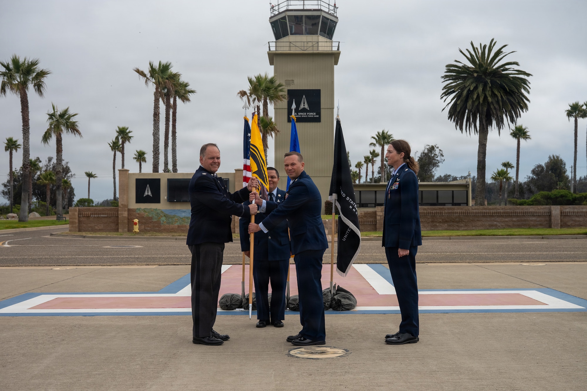 On an airfield with palm trees in the background the commander of Vandenberg passes the 30th OSS guidon to the next squadron commander with the former squadron commander standing behind.