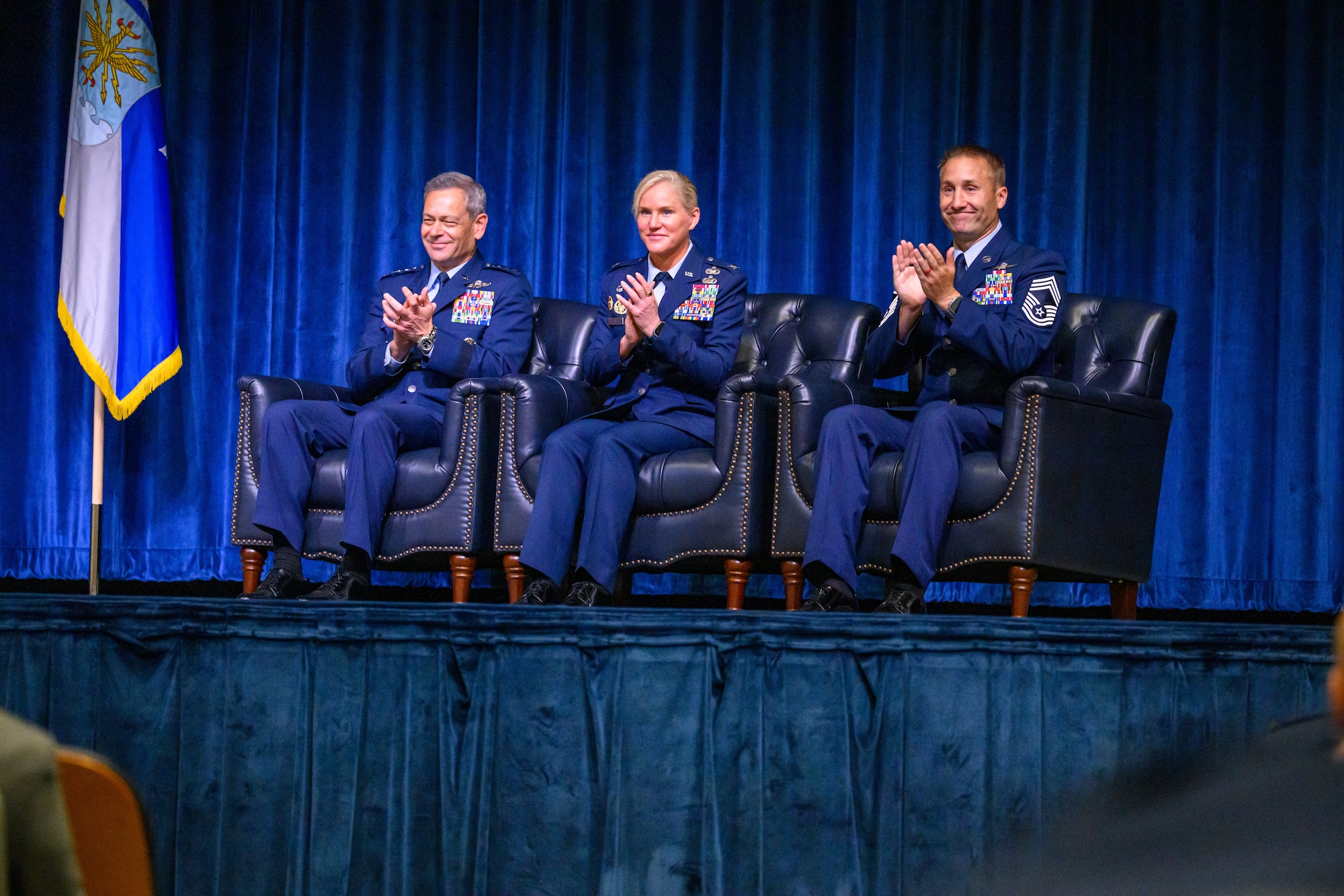 Three Servicemembers clap from on stage during a graduation ceremony