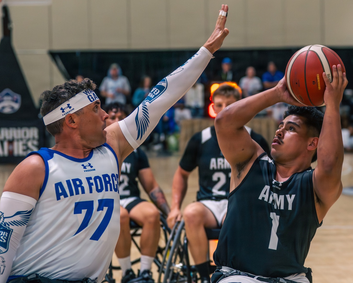 Two competitors are playing wheelchair basketball. One competitor is holding his arm up in front of the other competitor who is trying to shoot or pass the basketball.