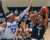 Two competitors are playing wheelchair basketball. One competitor is holding his arm up in front of the other competitor who is trying to shoot or pass the basketball.