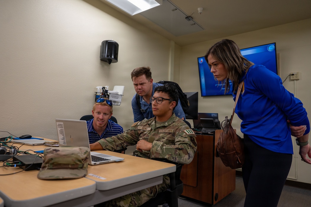 Four individuals look at a computer on a table