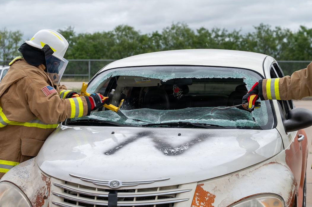 Two people in fire protective equipment saw through a windshield