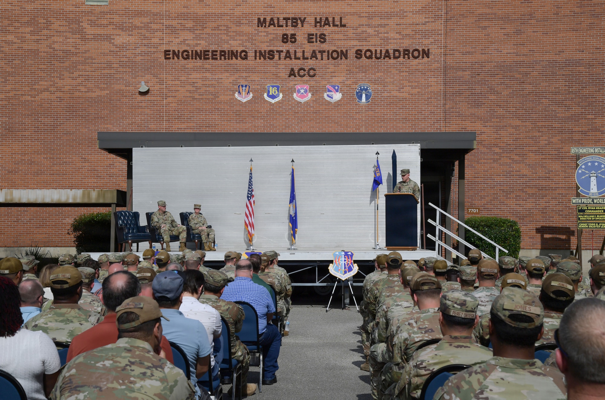 A stage is set outside in front of a group of people in chairs.