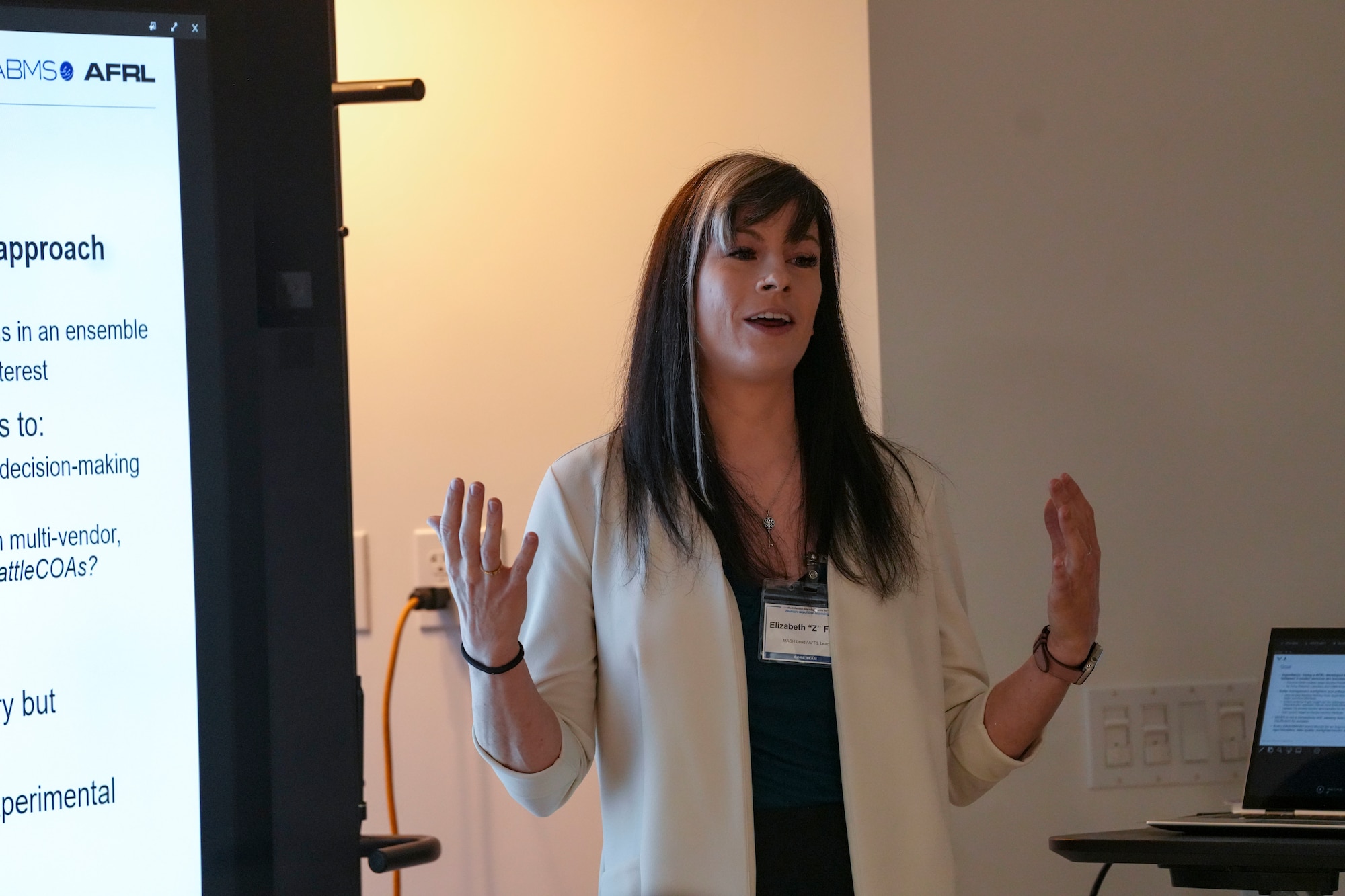 a woman stands in between two screens speaking