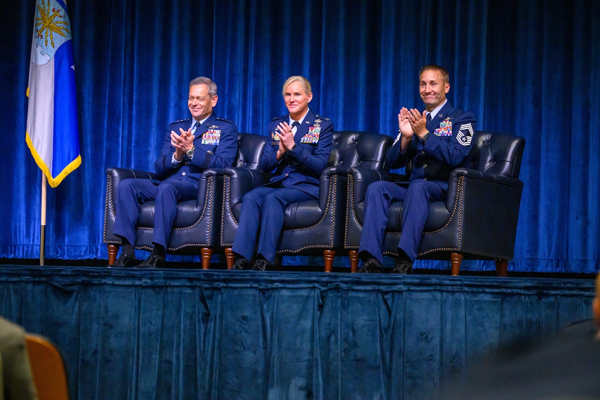Three Servicemembers clap from on stage during a graduation ceremony
