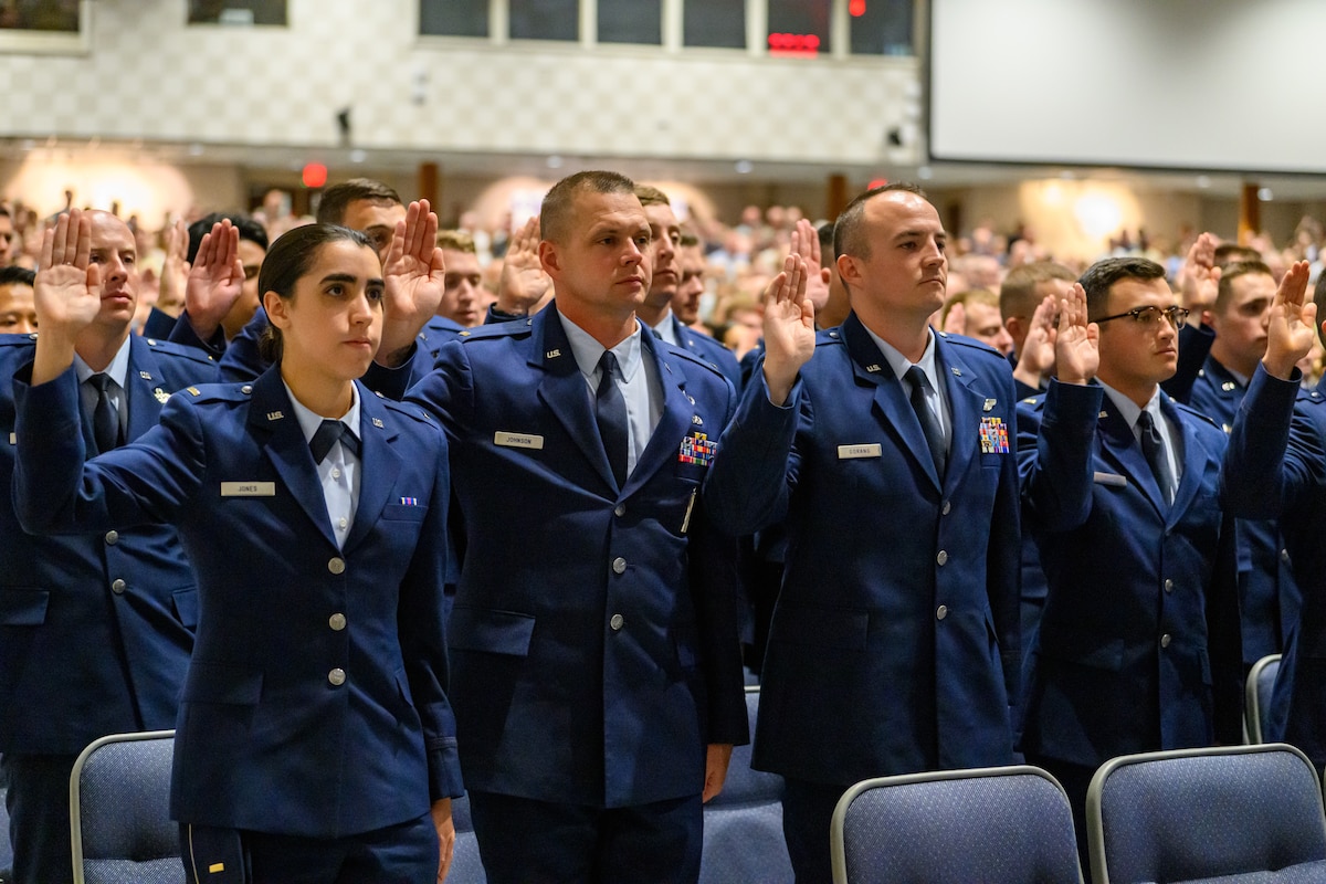 A group of servicemembers raise their hand to recite the oath of office during a  graduation ceremony
