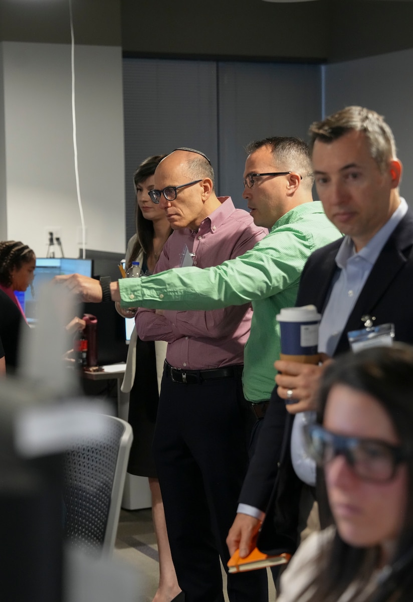 photo of people standing looking at people working on computers