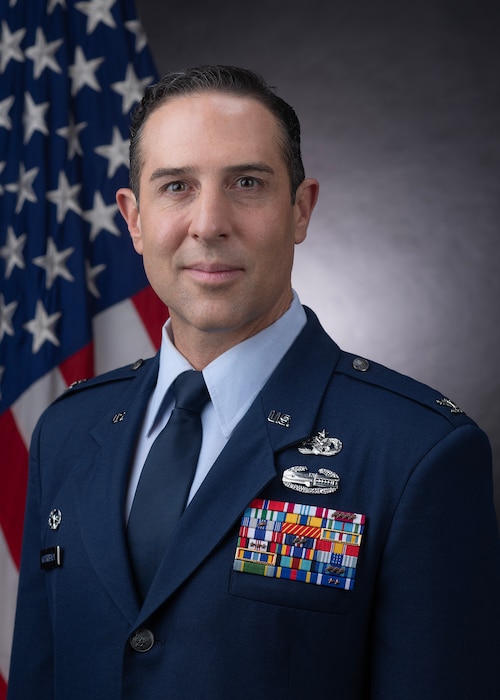 A person in a military uniform poses for a photo in front of an American flag.