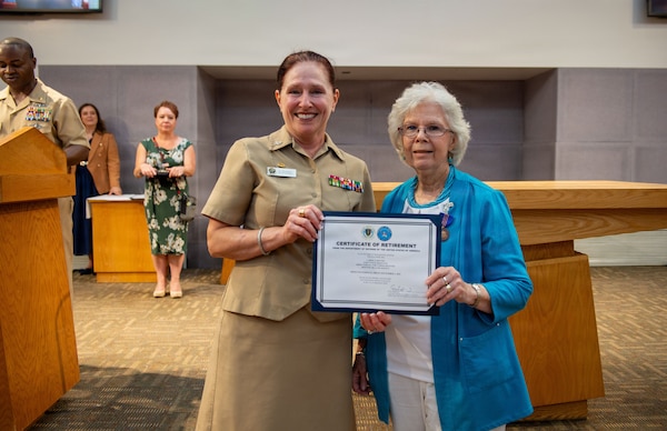 U.S. Navy Capt. Elizabeth Adriano, director, Naval Medical Center San Diego, presents a certificate of retirement to  Carol Devine, executive assistant to the executive officer at NMCSD, during her retirement ceremony, June 24, 2026. Devine retired after 59 years of federal service, including 49 years at NMCSD. Throughout her career, Devine provided steadfast administrative leadership and continuity to generations of military and civilian leaders. The mission of NMCSD is to optimize health and enhance readiness. NMCSD employs more than 5,500 active-duty military personnel, civilians, and contractors in southern California to deliver exceptional care afloat and ashore. (U.S. Navy photo by Mass Communication Specialist 1st Class Marcus Stanley)