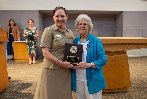 U.S. Navy Capt. Elizabeth Adriano, director, Naval Medical Center San Diego, presents a Civilian Career Service Award plaque to Carol Devine, executive assistant to the executive officer at NMCSD, during her retirement ceremony, June 24, 2026. Devine retired after 59 years of federal service, including 49 years at NMCSD. Throughout her career, Devine provided steadfast administrative leadership and continuity to generations of military and civilian leaders. The mission of NMCSD is to optimize health and enhance readiness. NMCSD employs more than 5,500 active-duty military personnel, civilians, and contractors in southern California to deliver exceptional care afloat and ashore. (U.S. Navy photo by Mass Communication Specialist 1st Class Marcus Stanley)