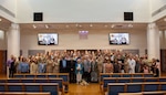 Carol Devine, executive assistant to the executive officer at Naval Medical Center San Diego (NMCSD), poses for a group photo with family members and retirement ceremony guests following her retirement ceremony at NMCSD, June 24, 2026. Throughout her career, Devine provided steadfast administrative leadership and continuity to generations of military and civilian leaders. The mission of NMCSD is to optimize health and enhance readiness. NMCSD employs more than 5,500 active-duty military personnel, civilians, and contractors in southern California to deliver exceptional care afloat and ashore. (U.S. Navy photo by Mass Communication Specialist 1st Class Marcus Stanley)