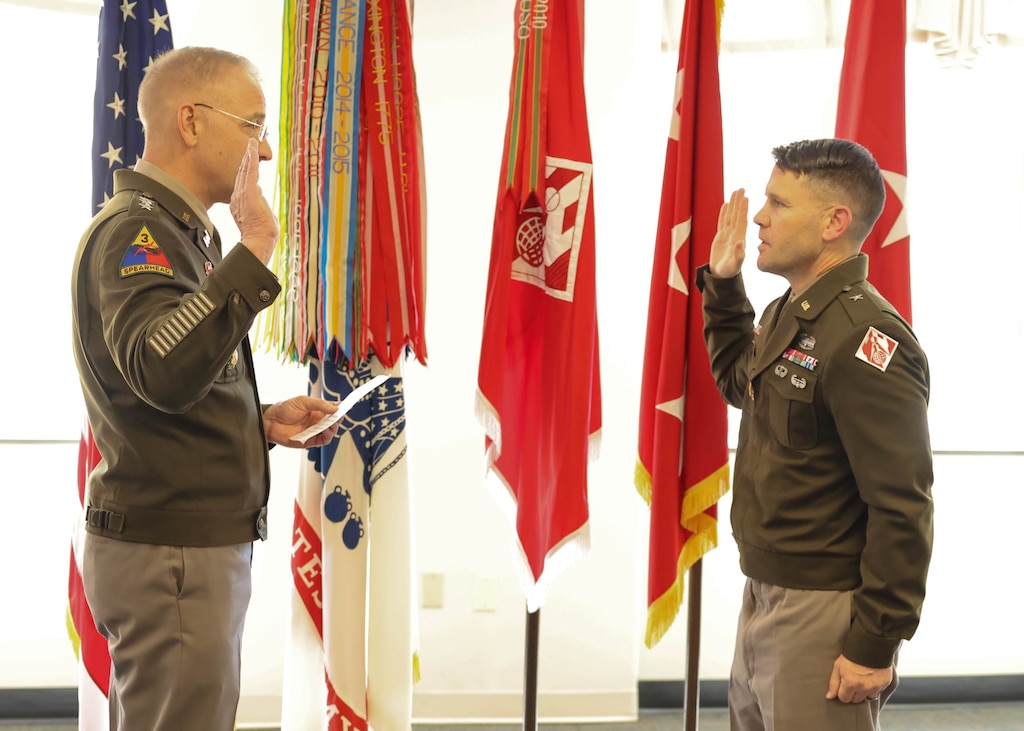 A man in an Army uniform administers an oath to another man in an Army uniform.