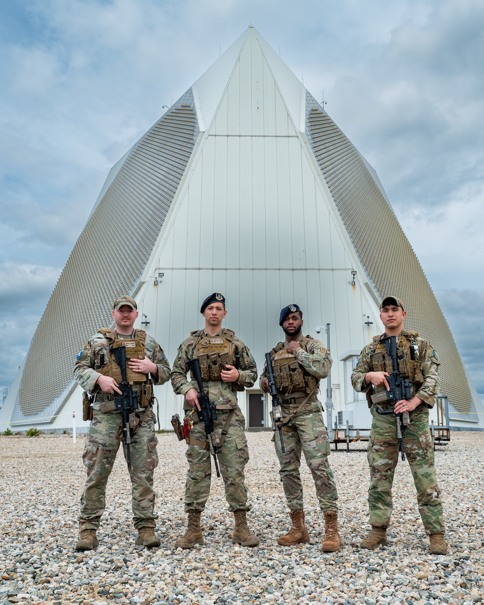 (from left) U.S. Air Force Senior Airman Blake Narrell, Staff Sgt. Christian Flores, Senior Airman Djey Dorgilus and Senior Airman Ian Aguilar, Security Forces members at the 6th Space Warning Squadron (6 SWS), pose in front of the Upgraded Early Warning Radar (UEWR) facility at Cape Cod Space Force Station, Massachusetts, May 9, 2024. 6 SWS, located at Cape Cod Space Force Station in Sagamore, Massachusetts, is a geographically separated unit of Space Delta 4, Buckley Space Force Base, Colorado. "Team 6" includes U.S. Space Force Guardians, U.S. Air Force and Royal Canadian Air Force Airmen and civilian employees. Their mission is "To surveil air and space to detect missile launches and high-interest satellites while operating, maintaining, and protecting New England’s first Space Force installation.” (U.S. Space Force photo by Dave Grim)