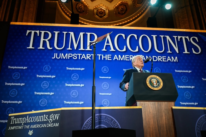 A man in business attire stands behind a lectern and speaks into a microphone. The screen behind him states, "Trump Accounts jumpstart the American Dream."