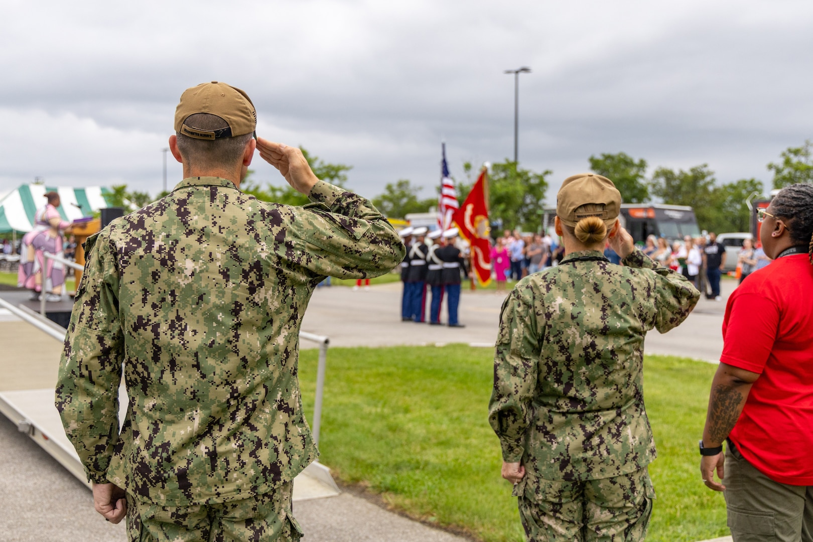 Back view of man and woman in military uniform saluting flag.
