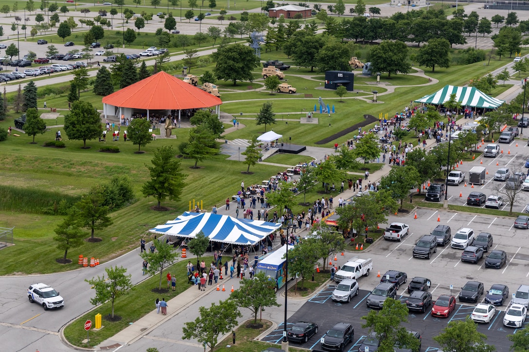 Overhead view of parking lot with two white and blue tents, lots of people and a pavilion with orange roof to the left