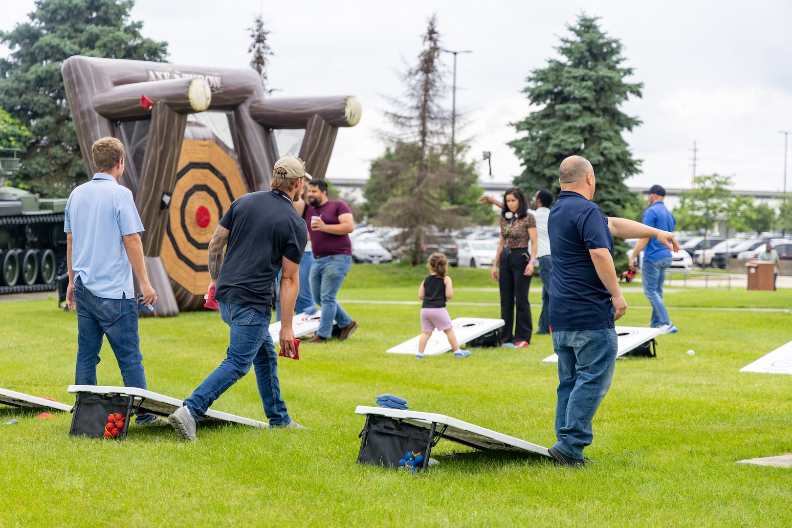 Several people playing cornhole in a grassy outdoor area.