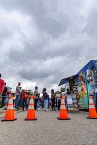 people standing in line at food truck with orange traffic cones in front