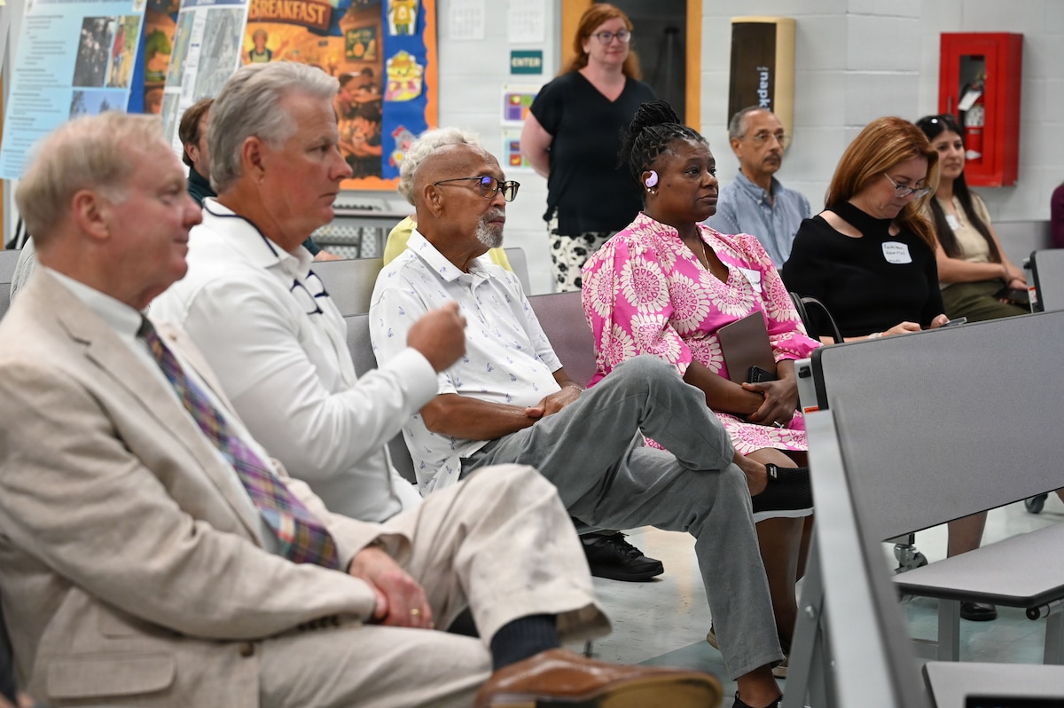 A crowd of people sit and listen to a speech.