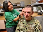 At the hearing clinic, a technician fits a hearing aid on a Soldier.