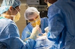 Surgeons in scrubs and masks operating on patient.