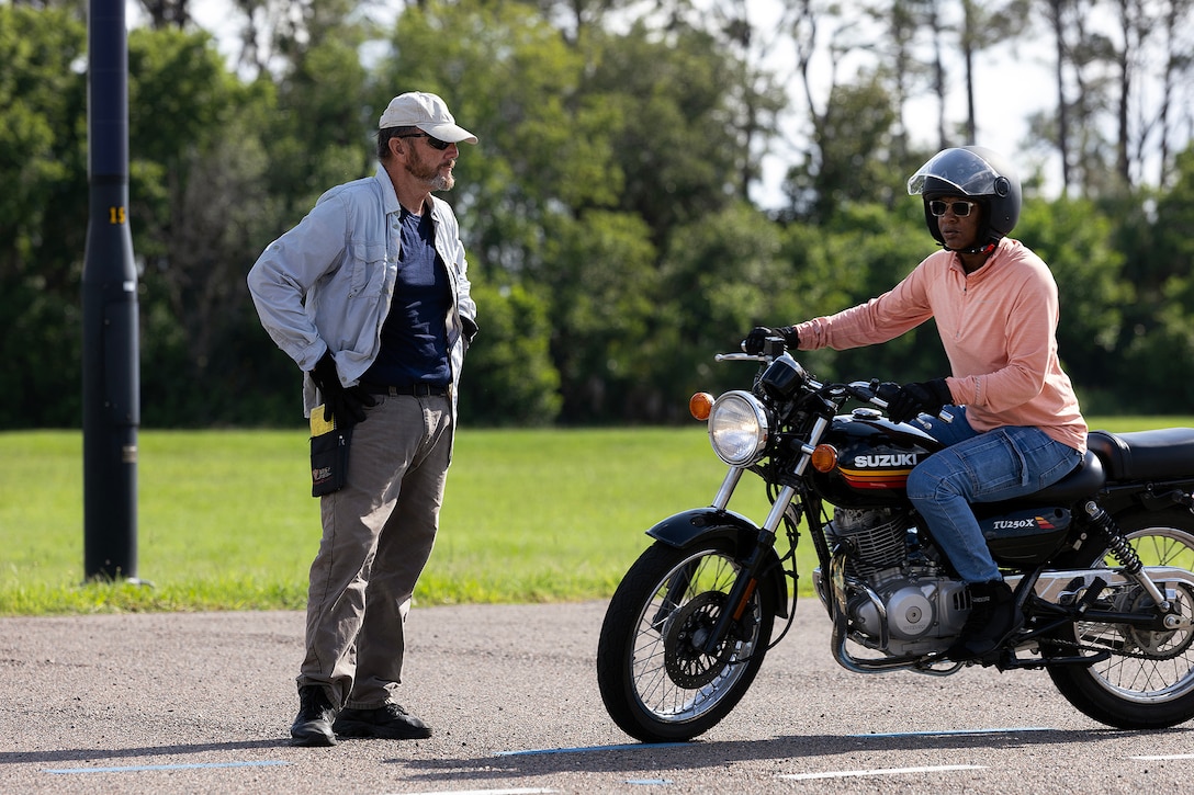 Retired Navy Chief Warrant Officer 4 Greg Wojciechowski, a Motorcycle Safety Foundation rider coach, watches Carletta McKenzie, a contracted supply material specialist for Blount Island Command, during a riding exercise in a basic rider course June 25, 2026, at Marine Corps Support Facility Blount Island, Florida. The two-day course equipped novice riders with classroom instruction and hands-on training to develop rider proficiency and promote motorcycle safety. (Marine Corps photo by Dustin Senger)