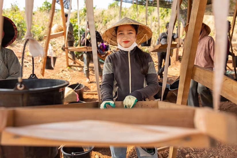 A woman wearing a conical hat stands in front of a wood tray.