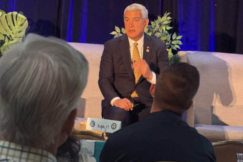 A man seated on a stage speaks to an audience.