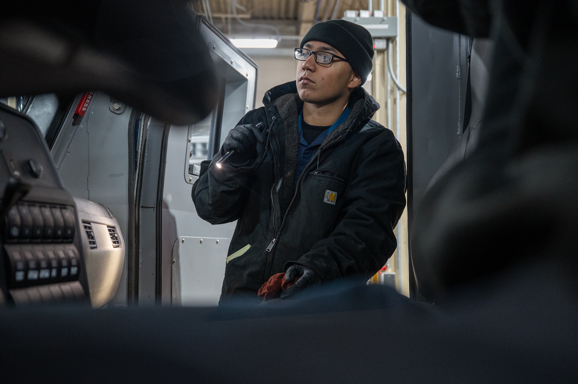 A man uses a flashlight to inspect a vehicle.