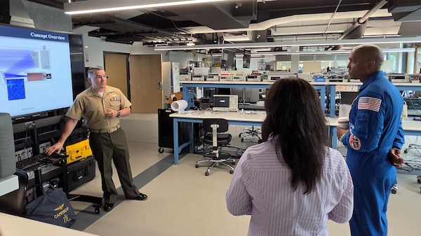 U.S. Marine Corps Lt. Col. Brian Neri, left, a former AV-8B Harrier pilot graduating from the space systems operations curriculum at the Naval Postgraduate School, briefs U.S. Navy Capt. Victor Glover about his thesis research on a space-based terahertz imaging camera that is scheduled to deploy to the International Space Station in early 2027. (U.S. Navy photo by Dan Linehan)