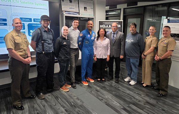 Naval Postgraduate School graduate U.S. Navy Capt. Victor Glover, center, stands with students, faculty, and staff from the Space Systems Academic Group following a series of research briefings from current students and a tour of the school’s small satellite laboratory and spacecraft operations center during a visit to campus, June 17, 2026. (U.S. Navy photo by Dan Linehan)