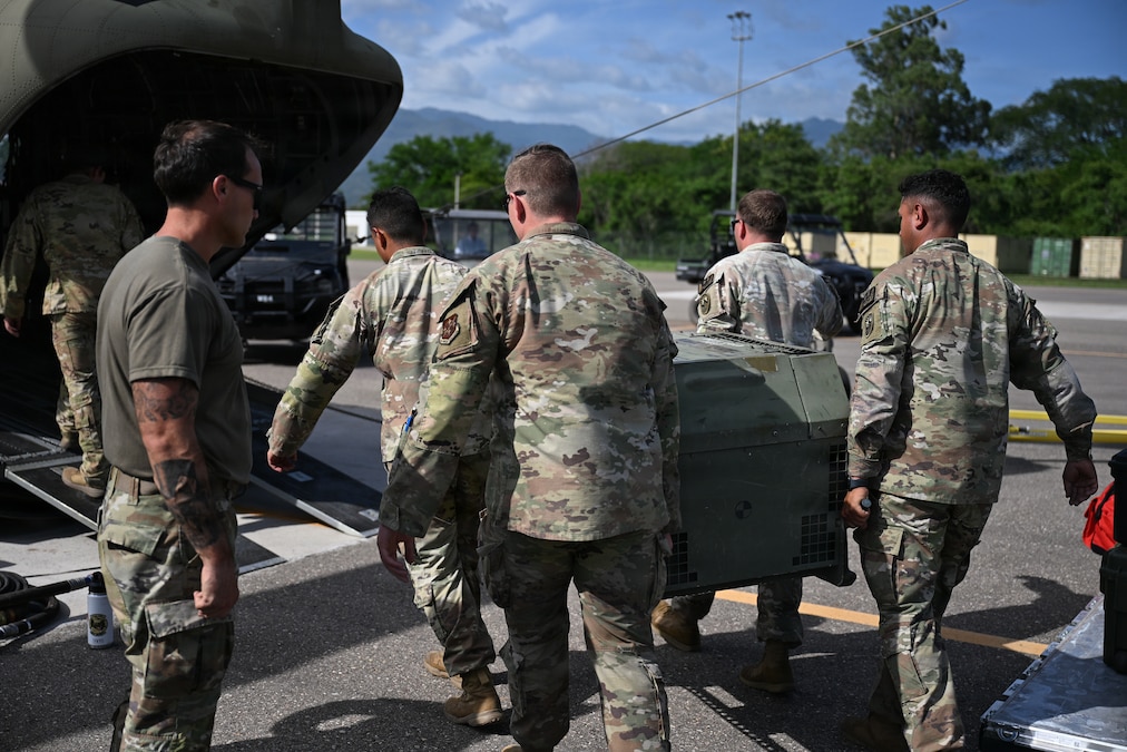 Military personnel load equipment onto a helicopter