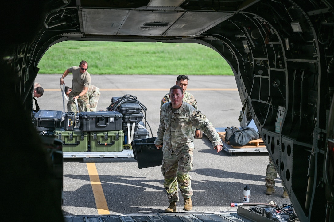 Military personnel load equipment onto a helicopter