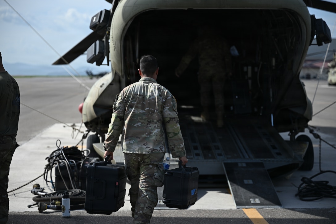 Military personnel load equipment onto a helicopter