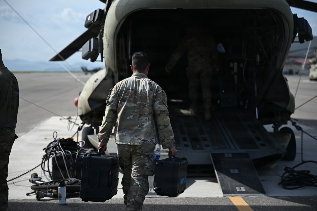 Military personnel load equipment onto a helicopter