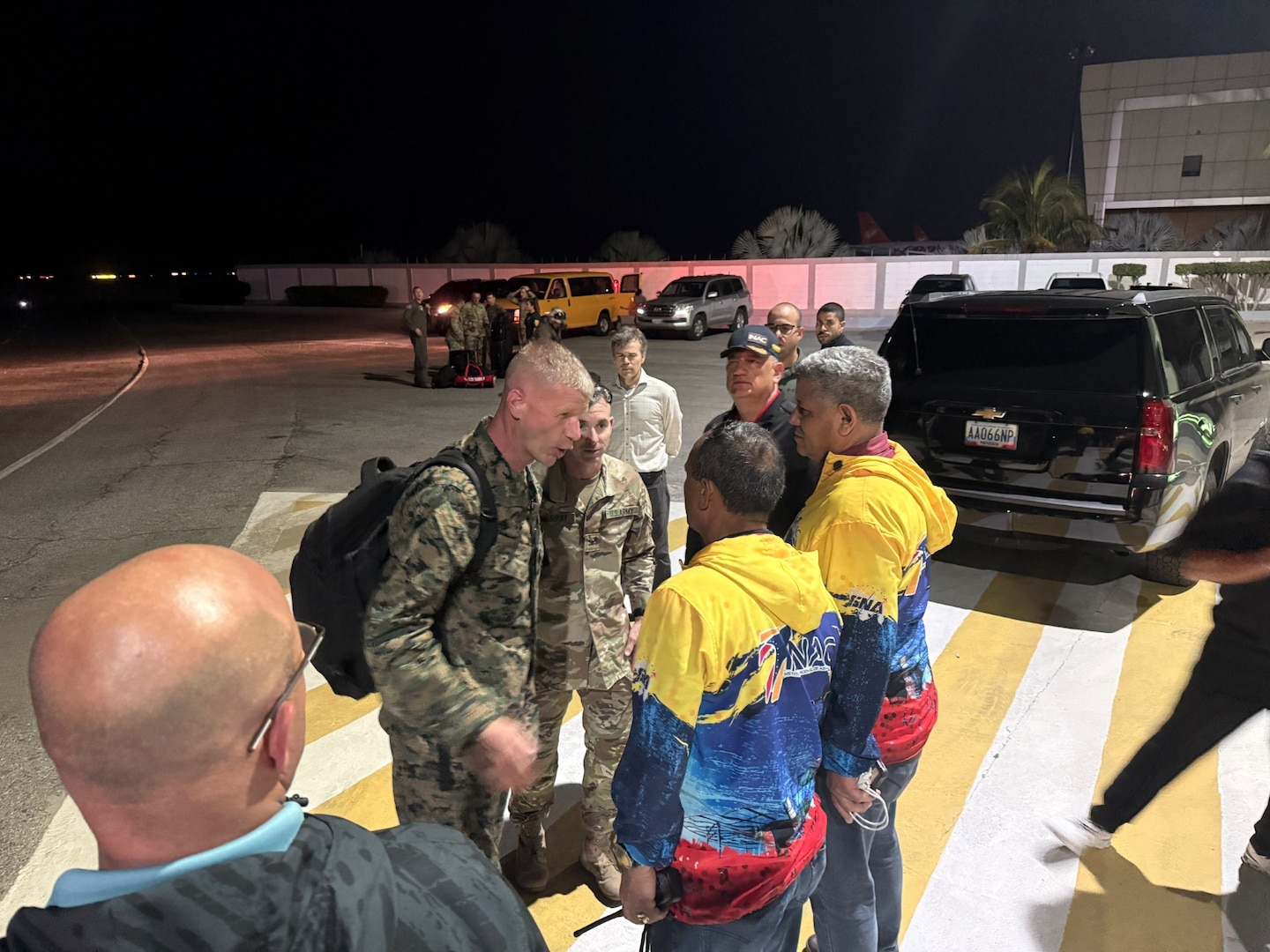A man in a military uniform talks with two men in red, yellow and blue jackets.